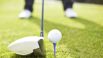 2 feet standing over a golf club positioned to hit a golf ball on a tee