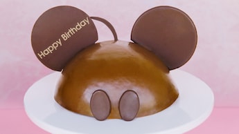 A chocolate cake designed to resemble Mickey Mouse, inscribed with the message 'Happy Birthday'