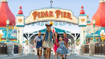 A young Guest in Minnie Ears leads her happy family through Pixar Pier