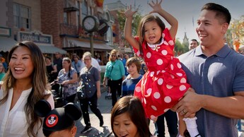 A young girl in a Minnie Mouse dress is carried by her father as their family walks down  Main Street USA
