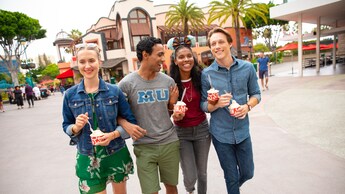 Cuatro jóvenes sonrientes caminan tomados del brazo por Downtown Disney District mientras sujetan copas de helado 