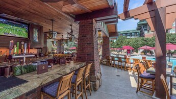 An outside bar with brick pillars and a flat screen television near a pool