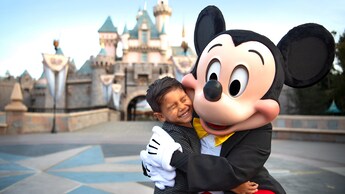 Mickey Mouse shares a hug with a happy young Guest in front of Sleeping Beauty Castle