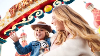 A mother holding her smiling son wearing a Woody cowboy hat in front of a marquee that says Pixar Pier