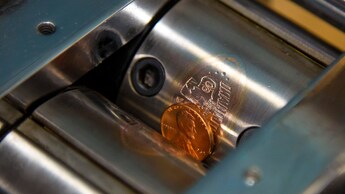 Una máquina de impresión de monedas con rodillos de acero graba un diseño de Disneyland Diamond Celebration en una moneda de un centavo