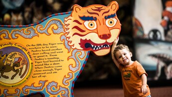 A little boy leans against a large stylized tiger cutout with a story written on it