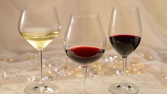 A glass of white wine next to a glass of red wine next to a glass of pinot noir