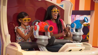 A young girl and a woman wearing special glasses to view the attraction, seated on a Carnival Ride Tram
