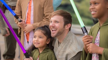 Un Jedi acompaña a una niña pequeña que sostiene un sable de luz de juguete