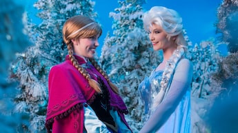 Los personajes de la Princesa Anna y la Reina Elsa sonríen de la mano rodeados de pinos nevados