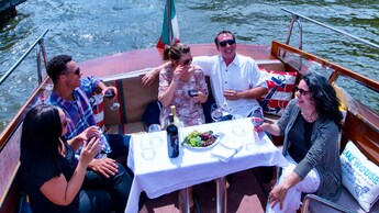 Cinq visiteurs sont assis autour d’une petite table à la poupe du Venezia et savourent des coupes de vin avec un plateau de fruits