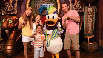 A mother, daughter, father and son posing with a snake-charmer-themed Donald at Magic Kingdom park