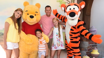 A mother, daughter, father and son posing with Winnie the Pooh and Tigger too at Magic Kingdom park