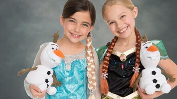 Duas meninas vestidas como Anna e Elsa segurando brinquedos de pelúcia do Olaf posam para um retrato no estúdio em frente a um cenário padrão