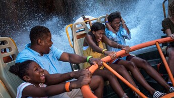 A laughing family getting splashed while riding the Kali River Rapids attraction, a river raft ride at Disney’s Animal Kingdom theme park