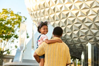 A father holding his smiling young daughter in his arms as he walks towards Spaceship Earth at Epcot