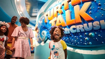 A man, woman and their 2 young children standing by a large sign that reads ‘Turtle Talk with Crush’