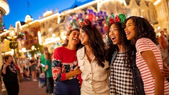 Cuatro mujeres, 2 de ellas con orejas de Mickey Mouse, sonríen en Main Street, U.S.A., en el Magic Kingdom theme park cerca de las decoraciones navideñas