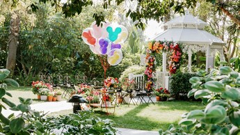 A garden wedding ceremony venue with a gazebo, floral arch, floral arrangements, chairs and Mickey Mouse balloons