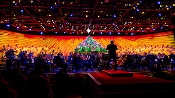 Una persona dirigiendo una orquesta y un coro; algunos miembros del coro están vestidos y dispuestos para verse como un árbol de Navidad en Candlelight Processional