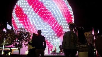 Los Visitantes de EPCOT miran a Spaceship Earth, que está encendida con rayas diagonales rosas y blancas