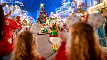 Daisy Duck dressed in festive attire, waving to Guests during a holiday parade at Magic Kingdom park