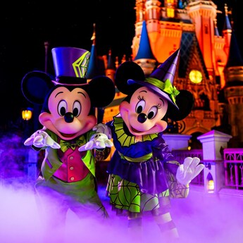 Minnie Mouse and Mickey Mouse wearing Halloween outfits and posing in front of Cinderella Castle
