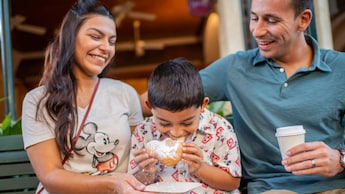 Dos padres sonríen mientras su hijo muerde en una beignet