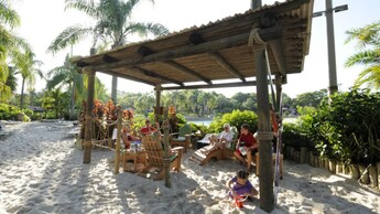 Une famille de six personnes assises dans des chaises Adirondack sous une structure en bois de style belvédère entourée de palmiers au parc aquatique Disney’s Typhoon Lagoon