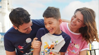 A boy and his parents wearing Walt Disney World tee shirts, laughing together near Cinderella Castle at Magic Kingdom park
