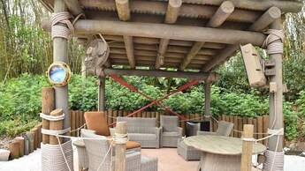 A covered outdoor lounge featuring a television screen, chairs and table at Disney’s Typhoon Lagoon water park