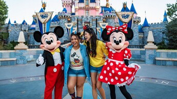 2 Guests pose with Mickey Mouse and Minnie Mouse in front of Sleeping Beauty Castle in Disneyland Park