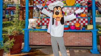 Goofy posing in a chef’s outfit with a kiosk of cookware at Disney’s California Adventure Park