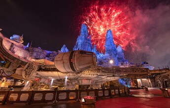 The Millennium Falcon docked in Star Wars Galaxy’s Edge at night with fireworks lighting up the sky