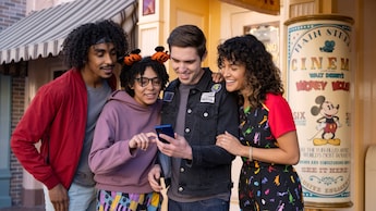 4 Visitantes mirando la pantalla de un teléfono mientras están de pie en Disneyland Park