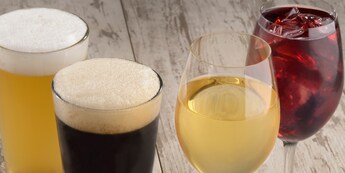 Four assorted beverages including a light beer, dark beer, white wine and red wine served in glasses on a wooden tabletop