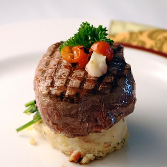 A steak served with creamy mash potatoes and garnished with a cherry tomato and parsley