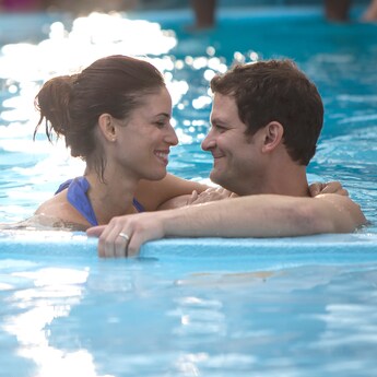 A man and a woman smile at each other in a swimming pool