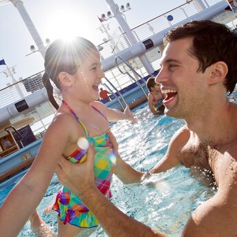 Um pai sorrindo para sua filha enquanto a levanta da água em uma piscina
