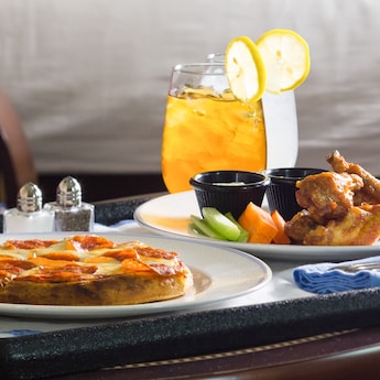 A meal consisting of pizza, chicken wings, cut vegetables with dipping sauce and an ice tea A meal consisting of pizza, chicken wings, cut vegetables with dipping sauce and an ice tea