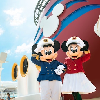 Captain Mickey Mouse and Captain Minnie Mouse waving their hands while standing next to the funnels of a Disney ship