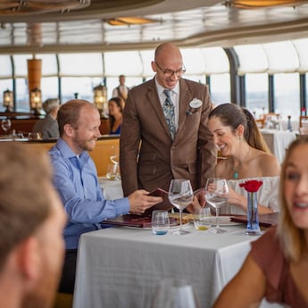 A waiter smiles while a couple reviews a menu in an upscale restaurant A waiter smiles while a couple reviews a menu in an upscale restaurant
