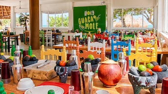 The cheerful interior of a restaurant, with a hanging sign that reads ‘Holy Guacamole’ and large windows that look out to the beach