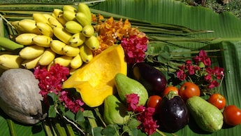Fresh, whole produce including bananas mangos, tomatoes and a coconut are laid out on a giant palm leaf