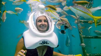 Una mujer sonriente con casco de buceo Sea TREK mira a distintos peces nadando a su alrededor