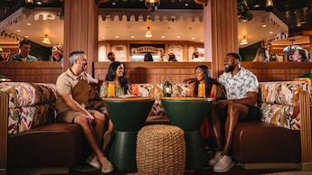 Guests smiling while sitting at tables with beverages at Skipper Society, a lounge on the Disney Treasure