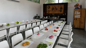 A cooking classroom featuring fresh produce sitting on the cutting board in front of each chair at long tables