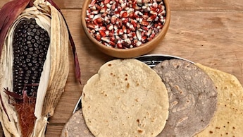 Bandeja de tortillas junto a un tazón de maíz y maíz en la mazorca