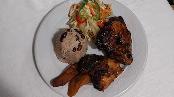 A plate of food with chicken, plantains, rice, a salad, and a tropical drink on the side