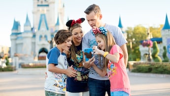 A family looks at a phone with Cinderella Castle in the background